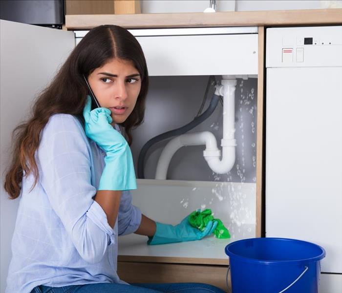 female catching water leak under a sink